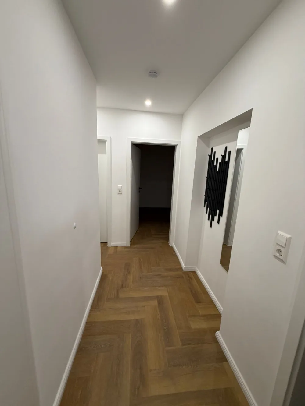Modernisierter Flur mit weißen Wänden, Fischgrätboden, neuen Türrahmen, Sockelleisten und moderner Beleuchtung
