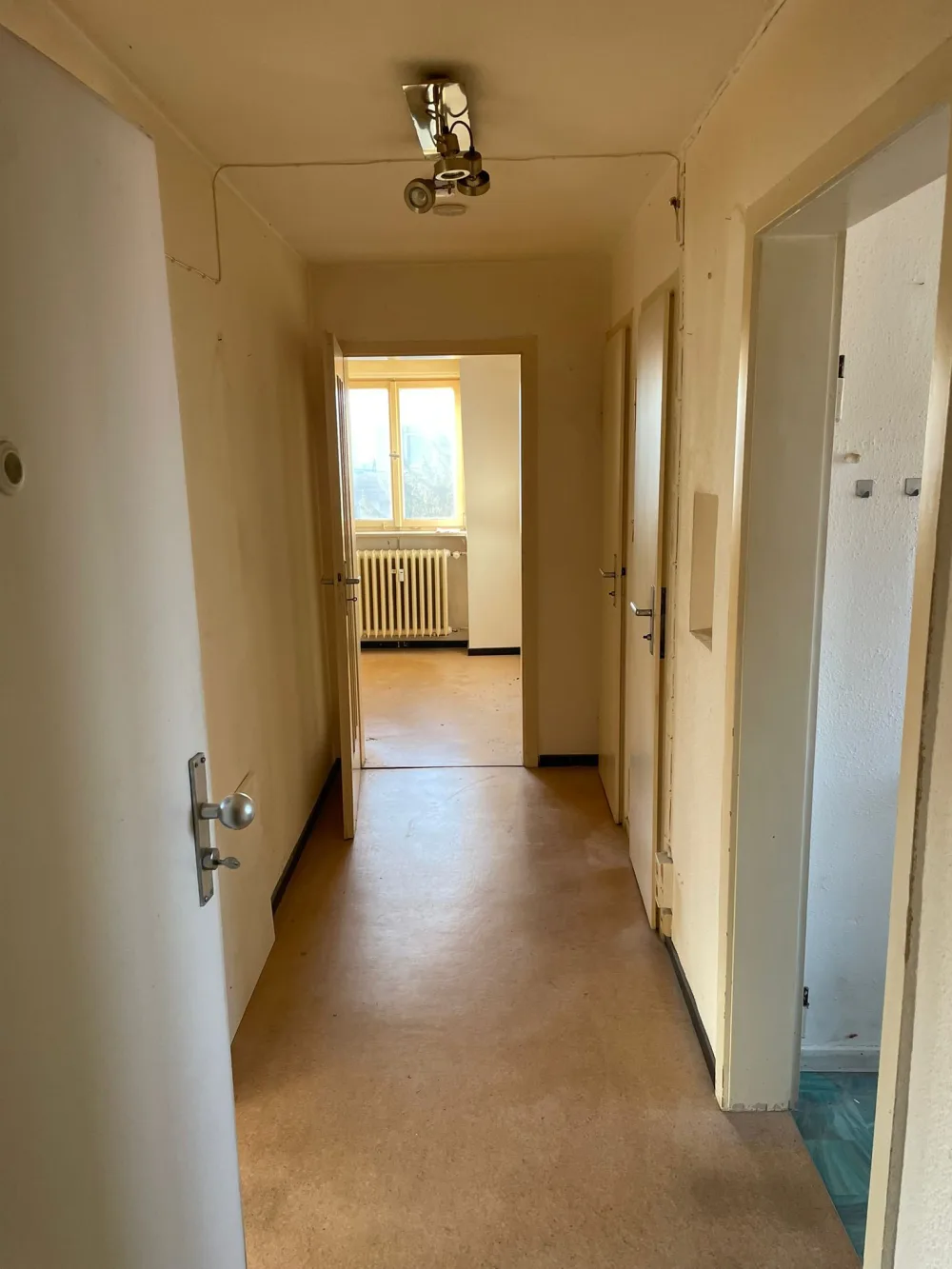 Flur vor der Renovierung mit alten Türen, abgenutztem Boden, vergilbten Wandflächen und veralteter Deckenleuchte
