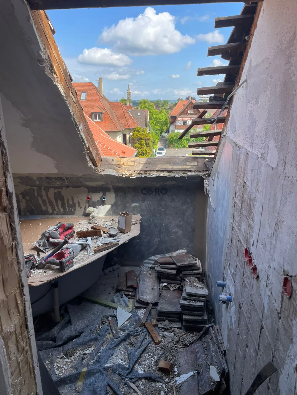 Dachgeschossbad vor der Sanierung mit geöffnetem Dachbereich, Bauschutt, alter Badewanne und rohen Wandflächen