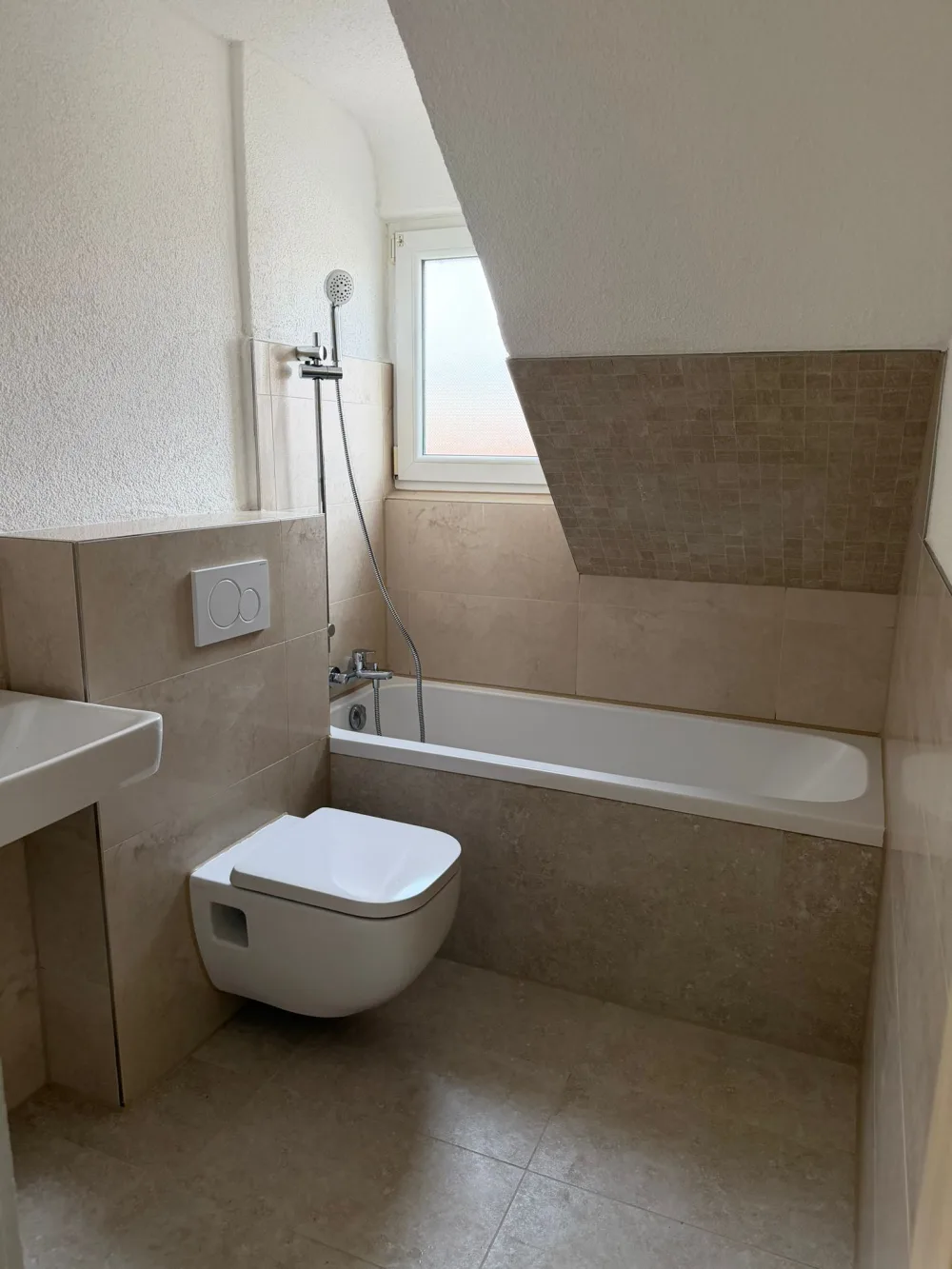 Modernisiertes Bad mit Glasdusche, grauen Fliesen, Holzoptik-Wand, schwarzer Armatur, Waschtisch und Fenster