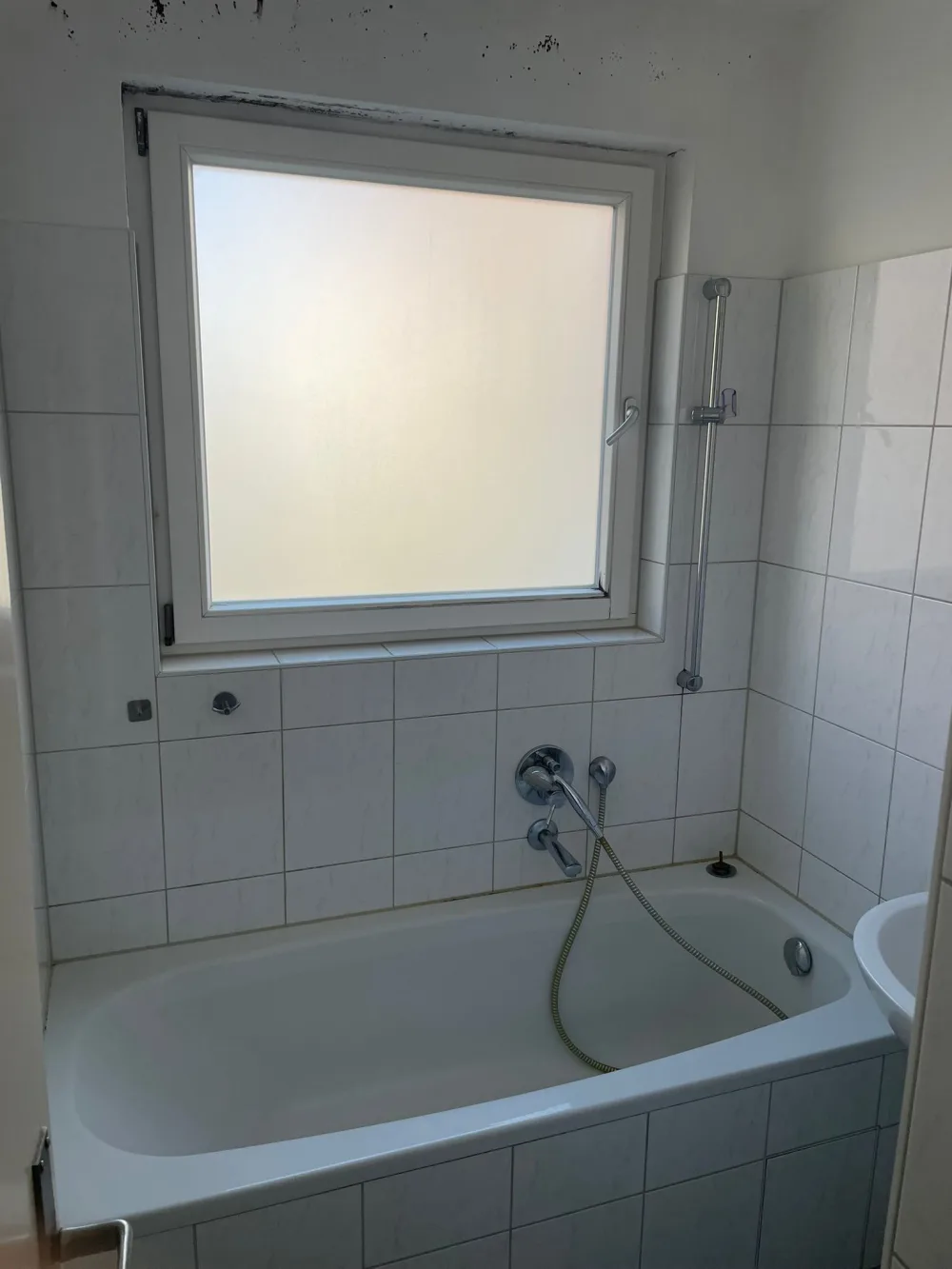 Bad vor der Modernisierung mit alter Badewanne, weißen Fliesen, Fenster und sichtbaren Gebrauchsspuren