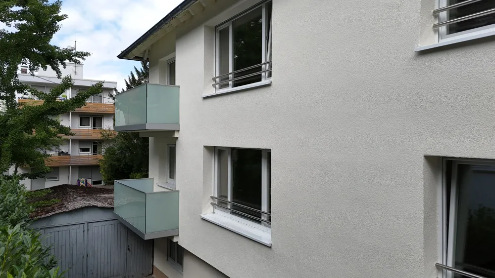 Modernisierte Hausfassade mit heller Putzfläche, Glasbalkonen, sauberen Fensteranschlüssen und gepflegter Außenansicht