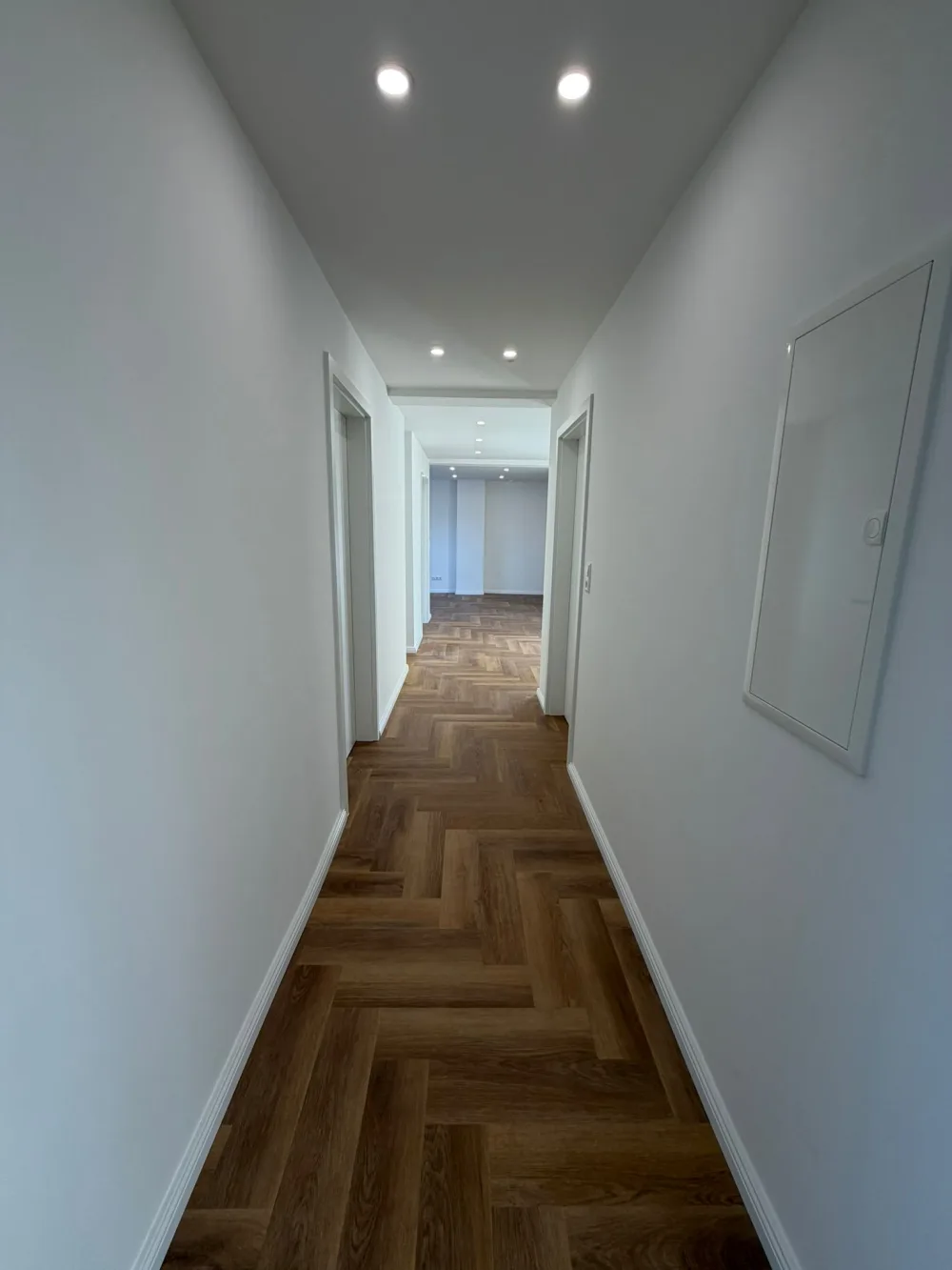 Modern ausgebauter Dachgeschossflur mit weißen Wänden, Fischgrätboden, Türen, Sockelleisten und Deckenspots