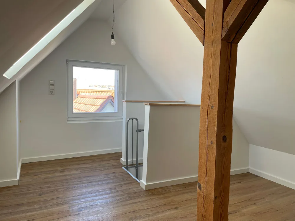 Modernisiertes Dachgeschoss mit hellen Wänden, Holzoptik-Boden, sauberer Fensterlaibung und sichtbarer Holzkonstruktion